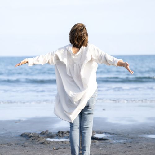 Vrouw op een strand met haar armen gespreid.